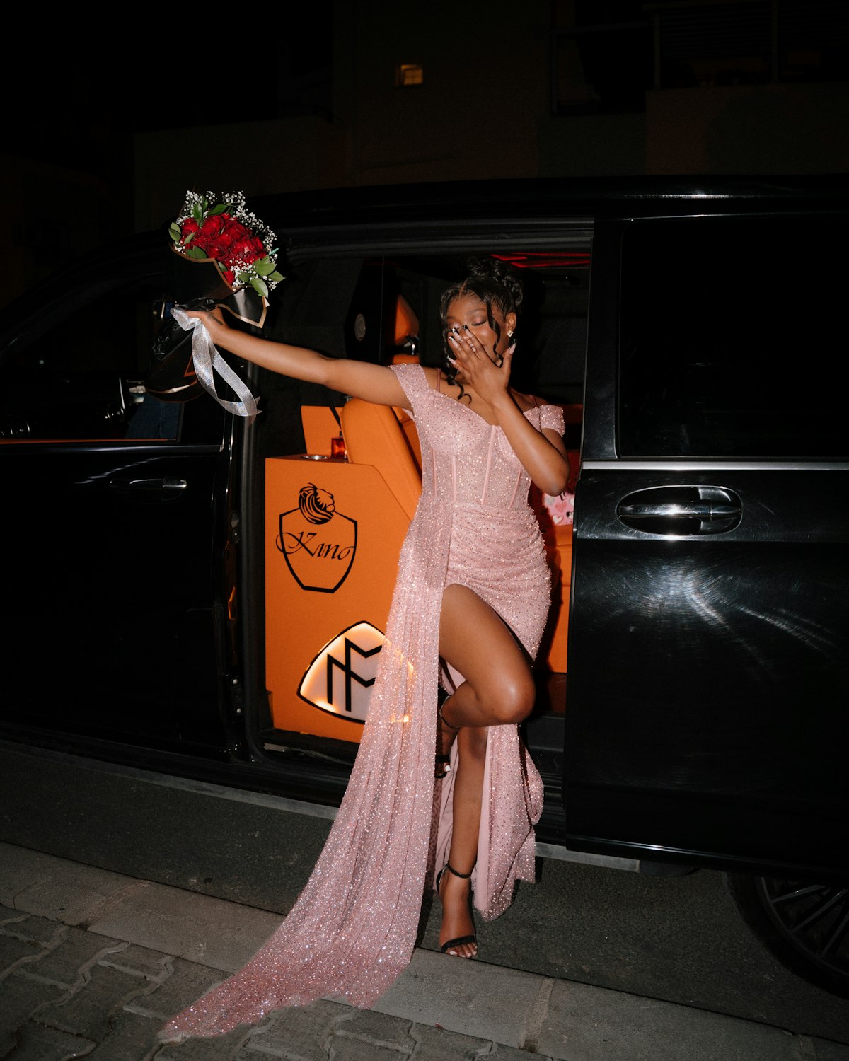 Young woman in a gown exiting a black car at night